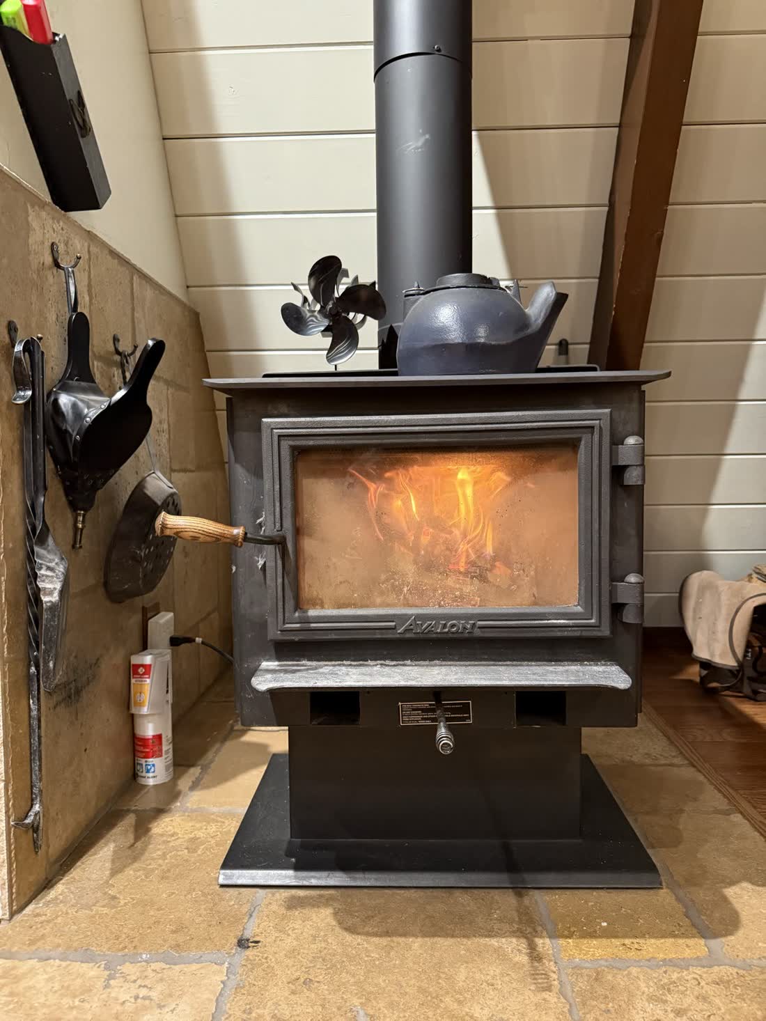 The stove glowing with a full fire, kettle and fan on top