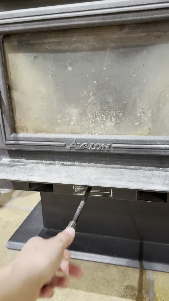 A hand pulling the air control rod out from under the stove door